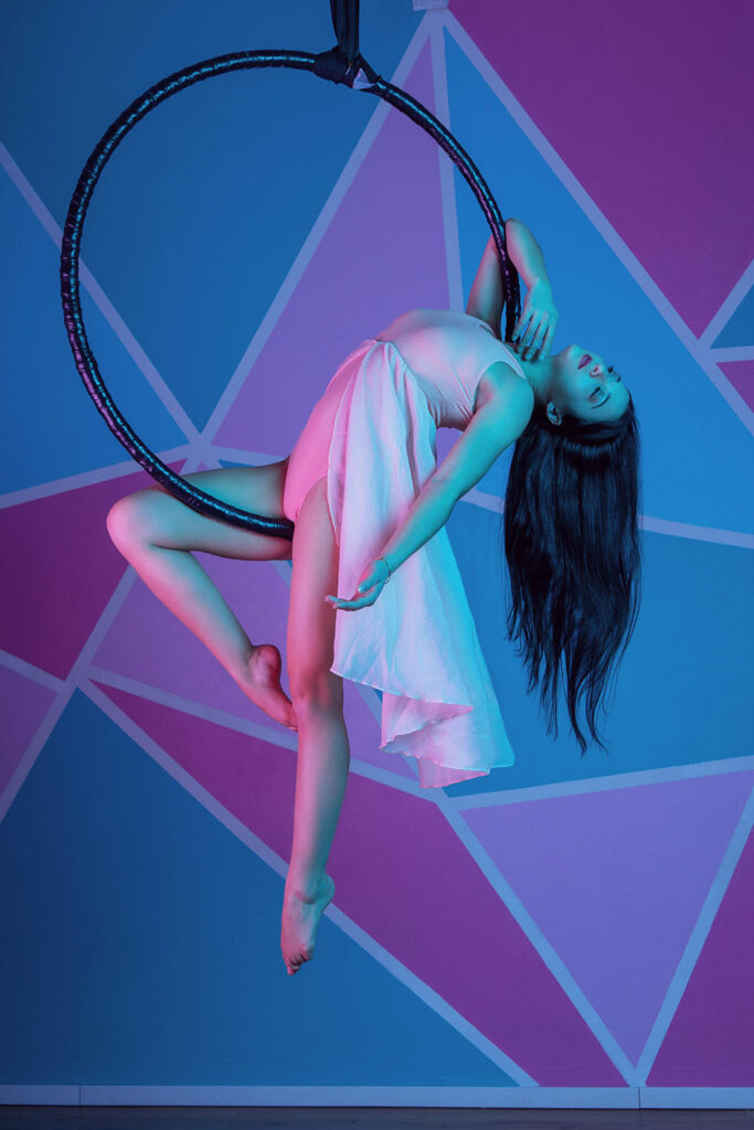 posed aerialist photo on aerial hoop, pink dress, long hair, arched back, bare foot, geometric background 