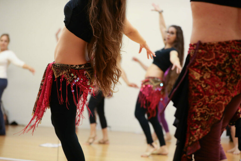 women in a bellydance class with black tops, black leggings and red hip scarves
