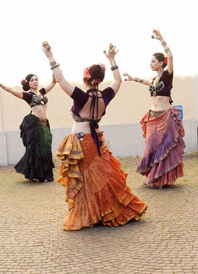 three women belly dancing, standing in a circle wearing black tops and colorful skirts playing finger cymbals 
