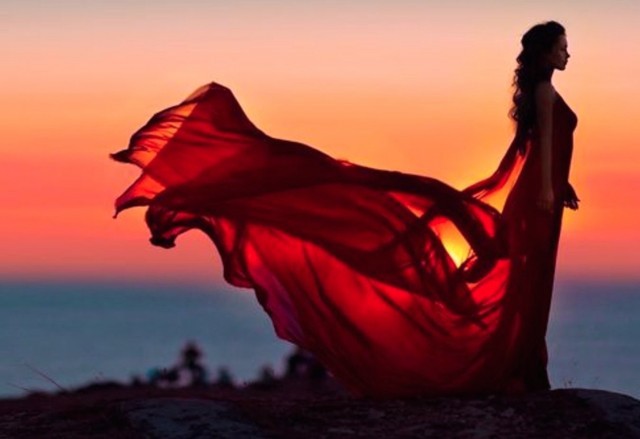 woman in a dress standing in a sunset with a flowing veil behind her