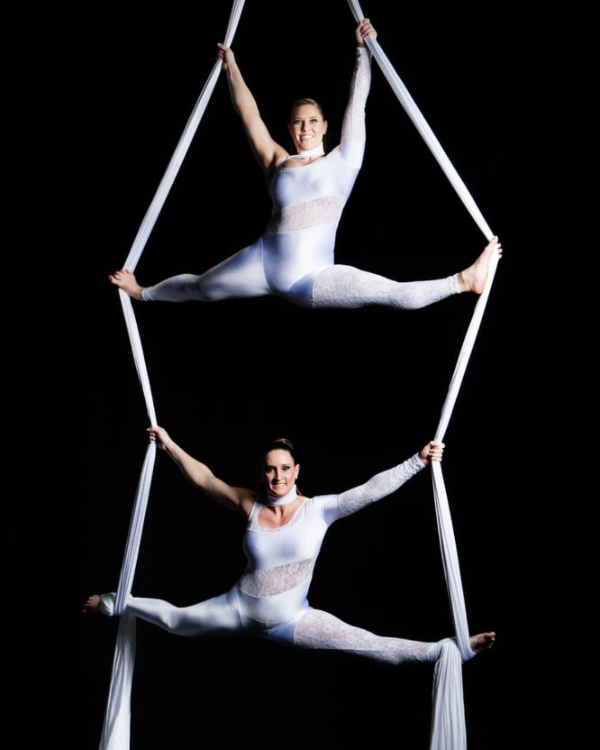 two aerialists in white unitards doing slits on white aerial silks